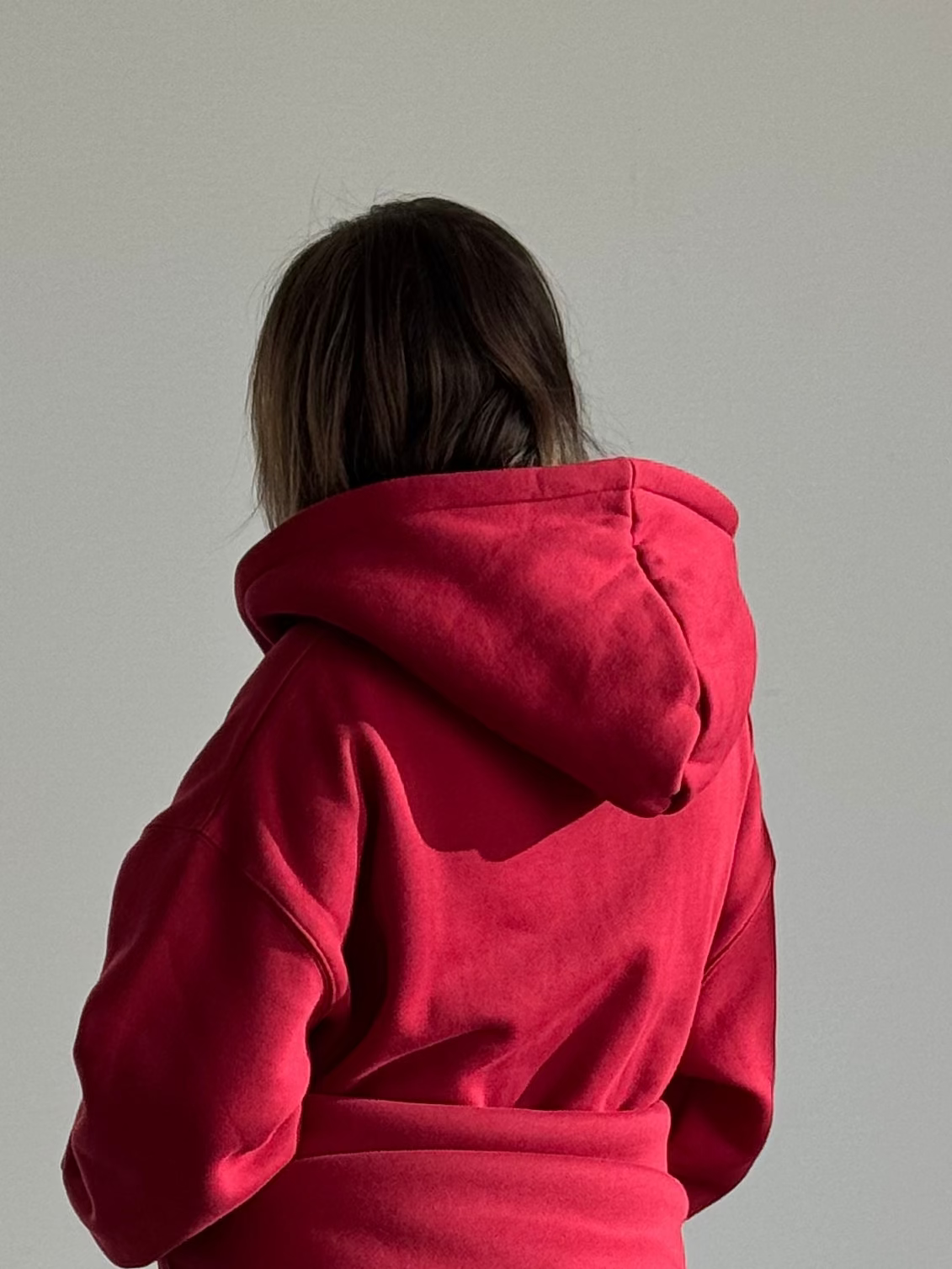 Person wearing a red hoodie and pants standing in a room with a mirror and chair.
