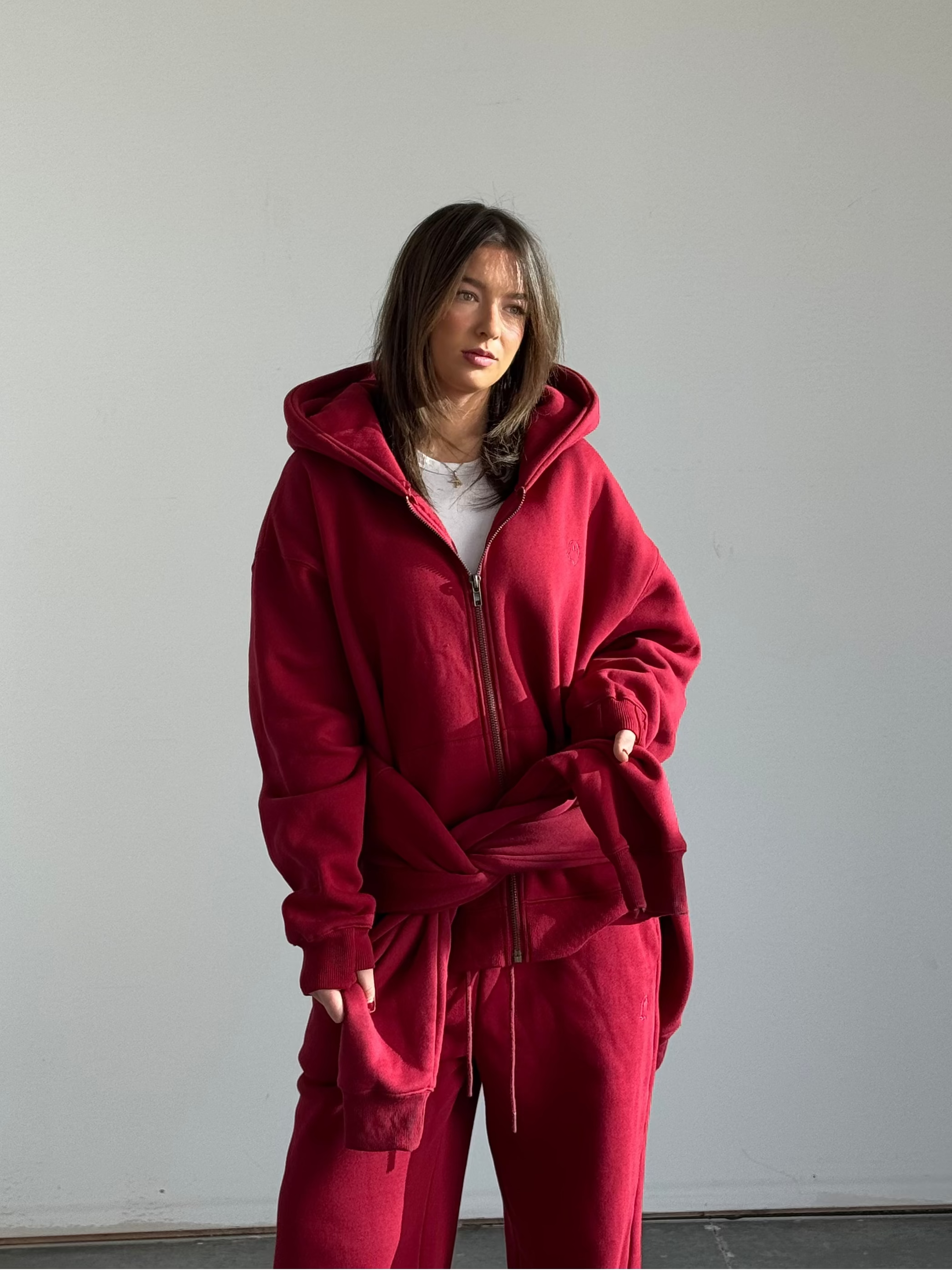 Person wearing a red tracksuit standing against a plain white wall.