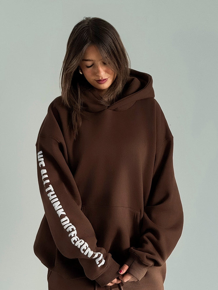 Person wearing a brown hoodie with text on sleeves against a plain background