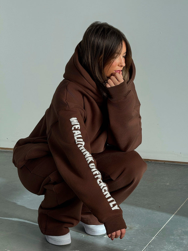 Person wearing a brown hoodie with text on the sleeve, sitting on a gray floor.