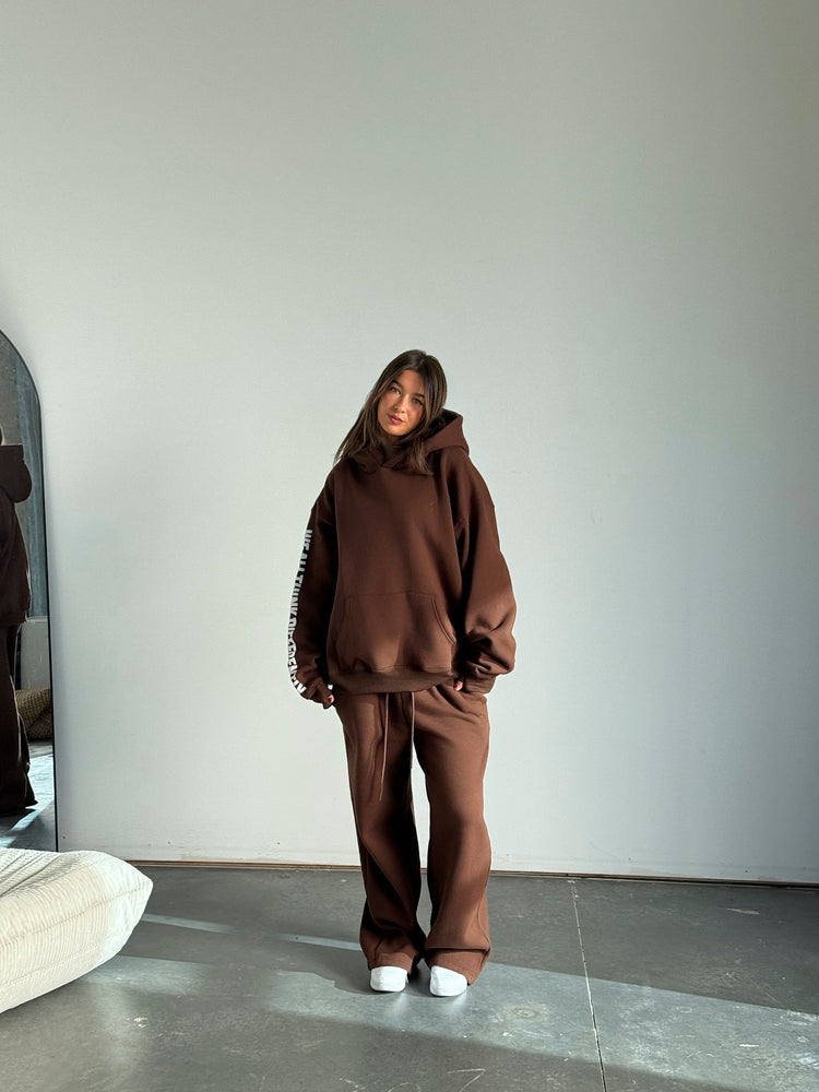 Person wearing a brown tracksuit standing against a plain white wall.