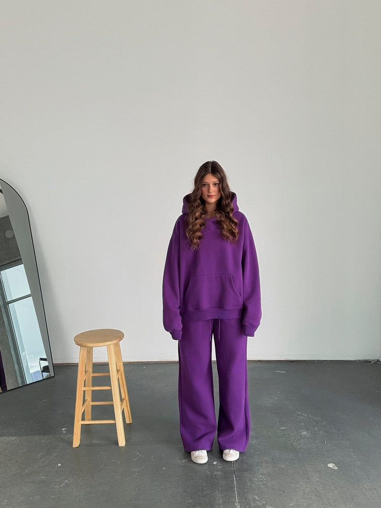 Person wearing a purple outfit standing in a minimalistic room with a mirror and stool.