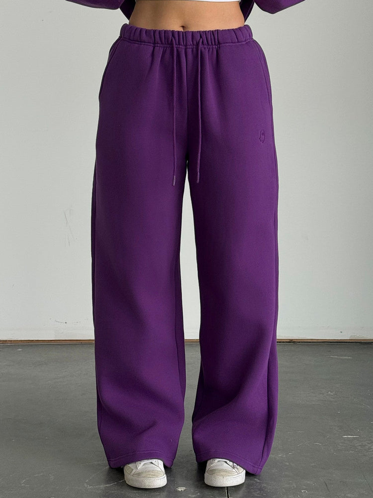 Person wearing a purple outfit with wide-leg pants and a cropped top against a plain background