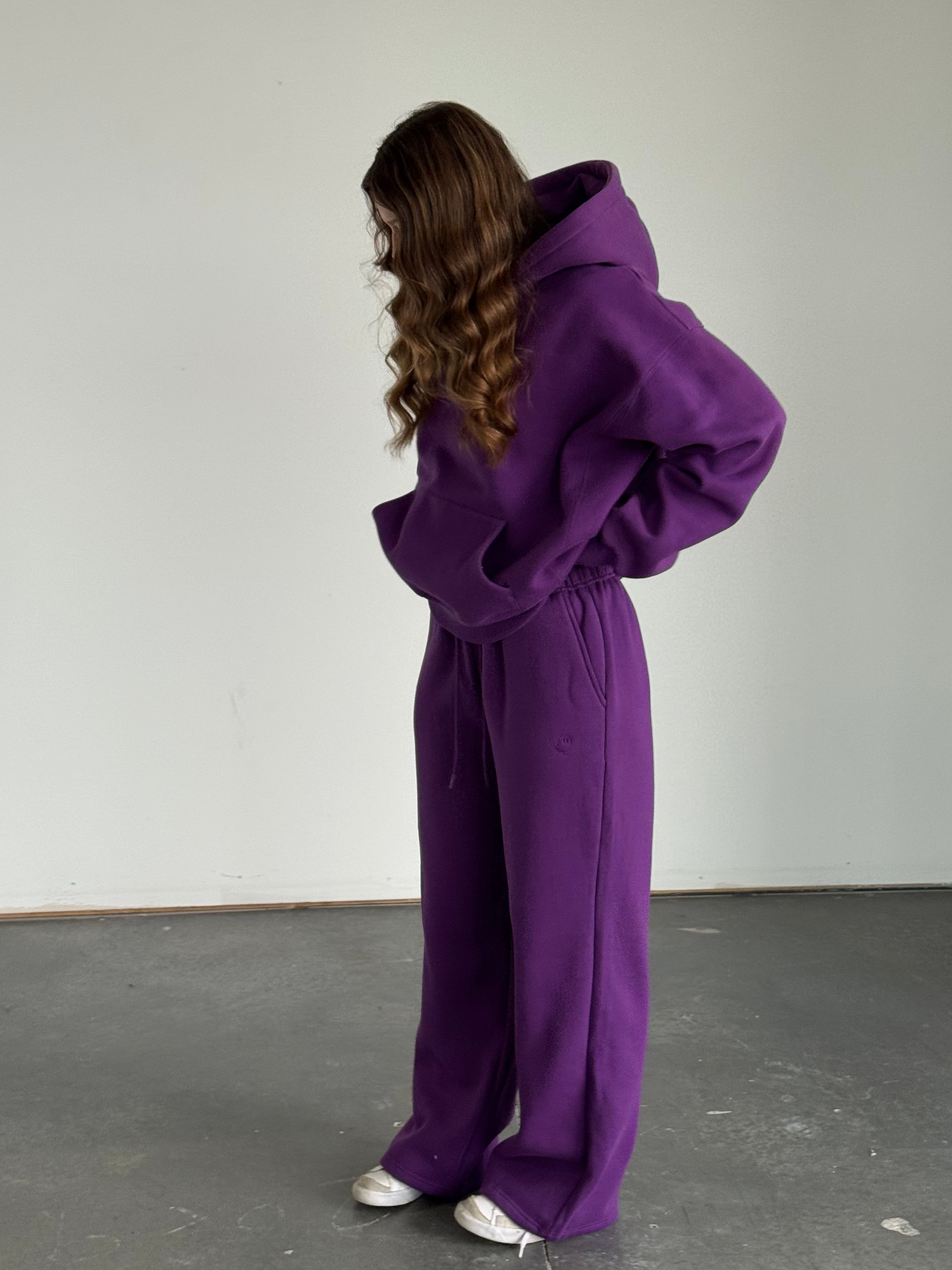 Person wearing a purple outfit standing in an indoor setting with a plain background