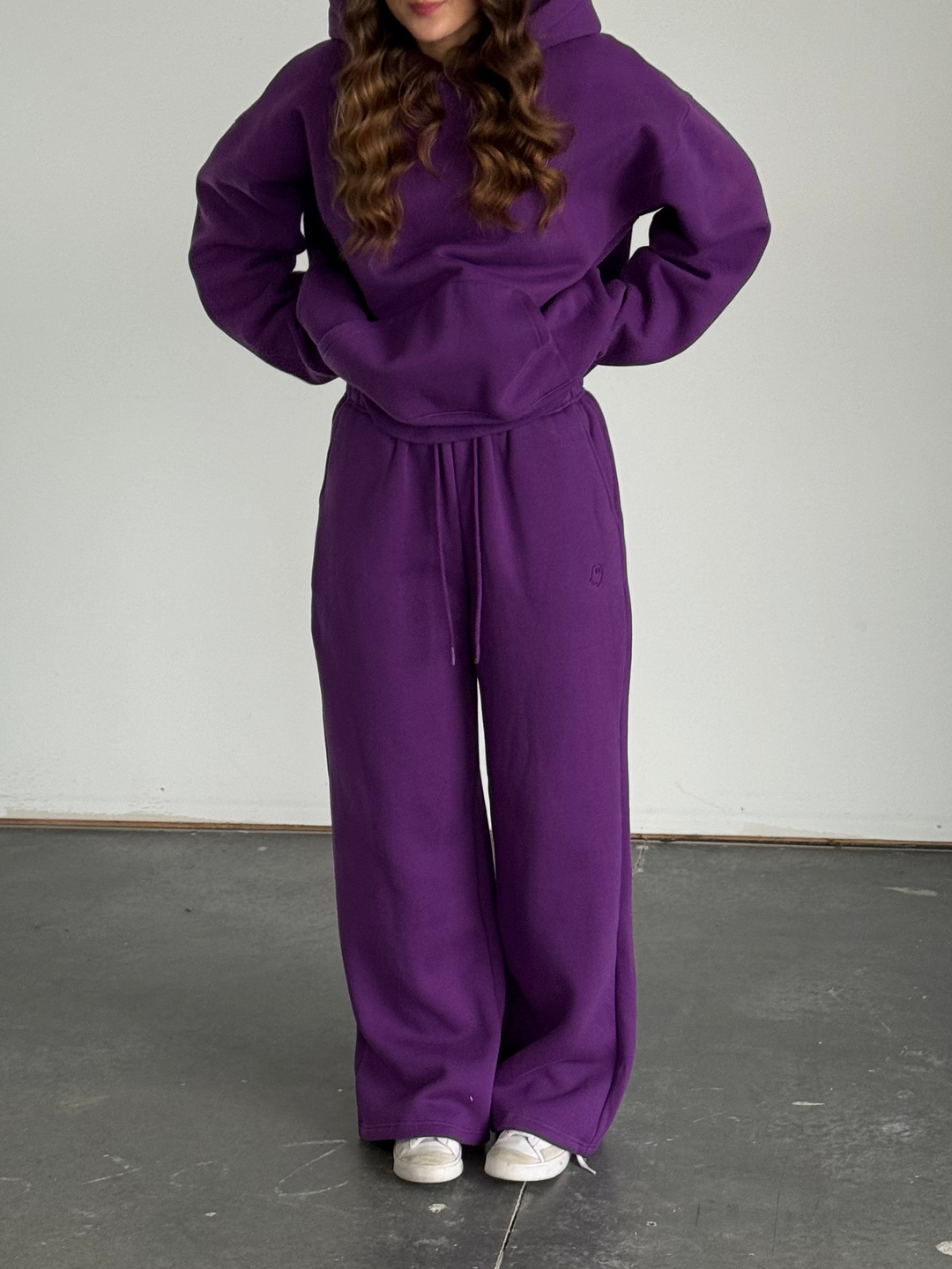 Person wearing a purple tracksuit standing against a plain background