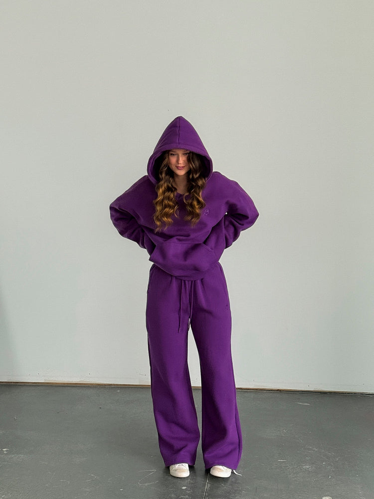 Person wearing a purple hoodie and pants set against a plain background