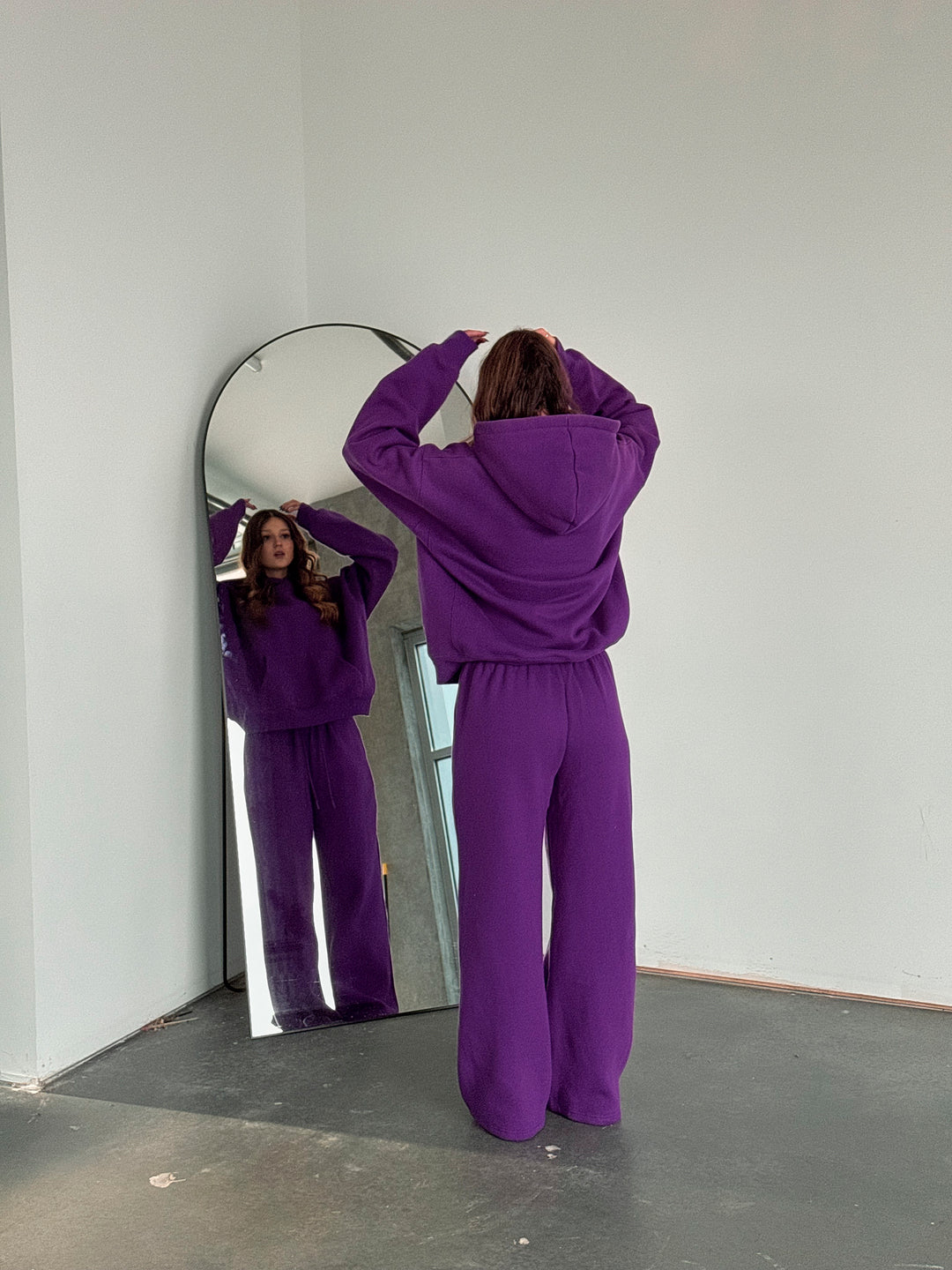 Person wearing a purple tracksuit standing in front of a mirror.