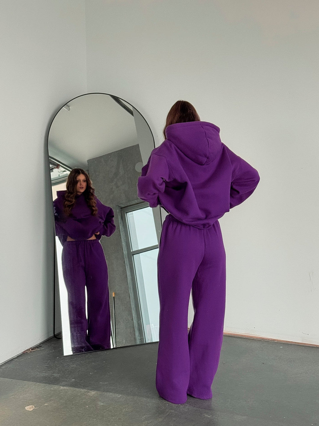 Person wearing a purple tracksuit standing in front of a mirror.