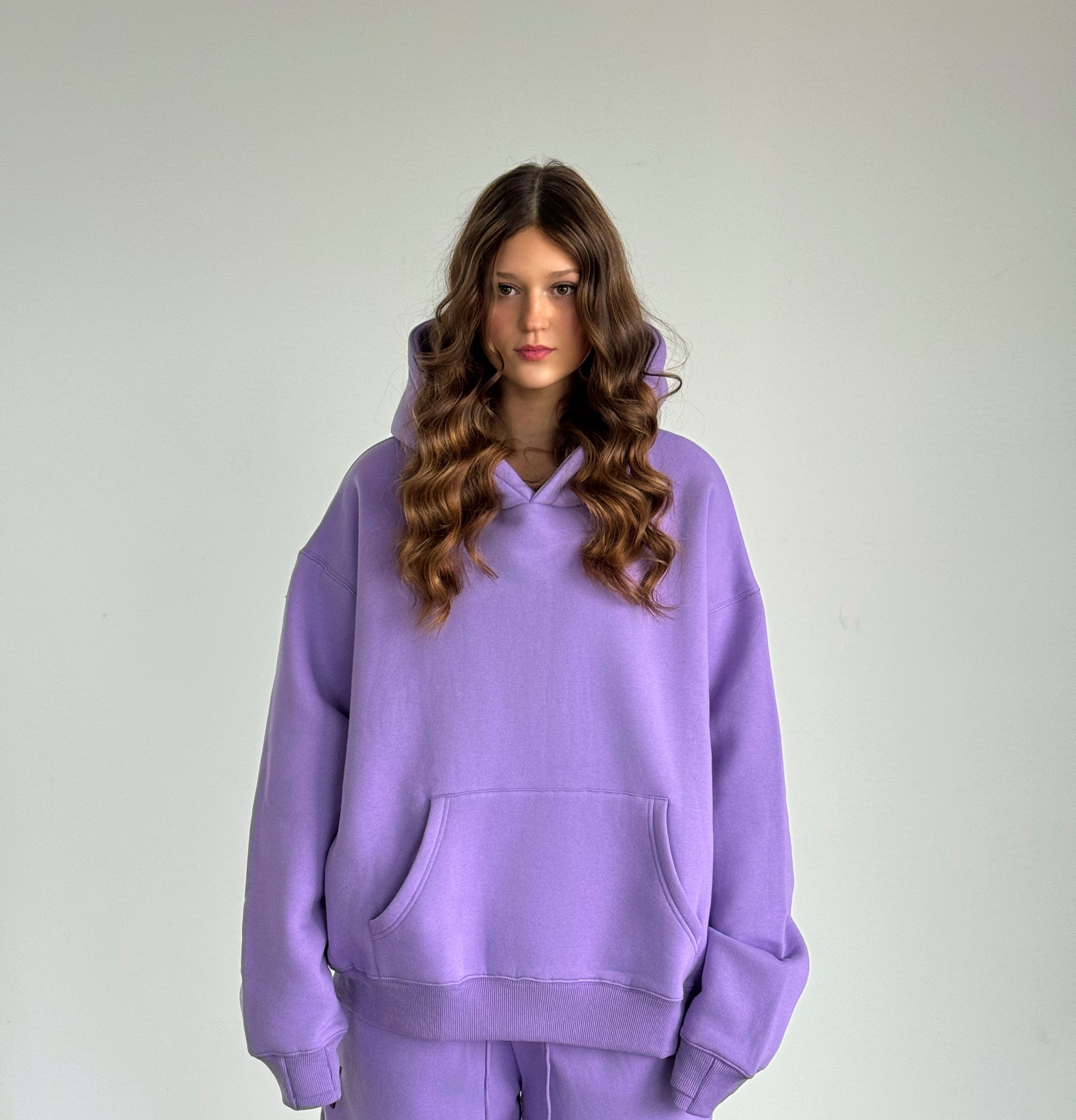 Person wearing a purple hoodie and pants against a plain background
