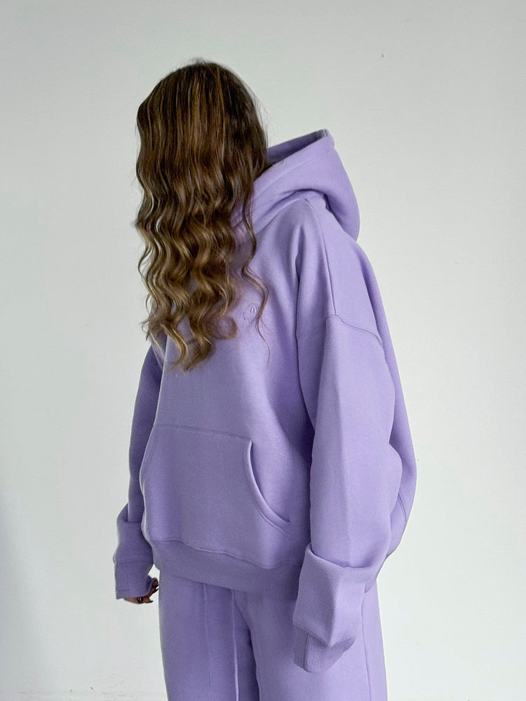 Person wearing a purple hoodie and pants in a minimal indoor setting