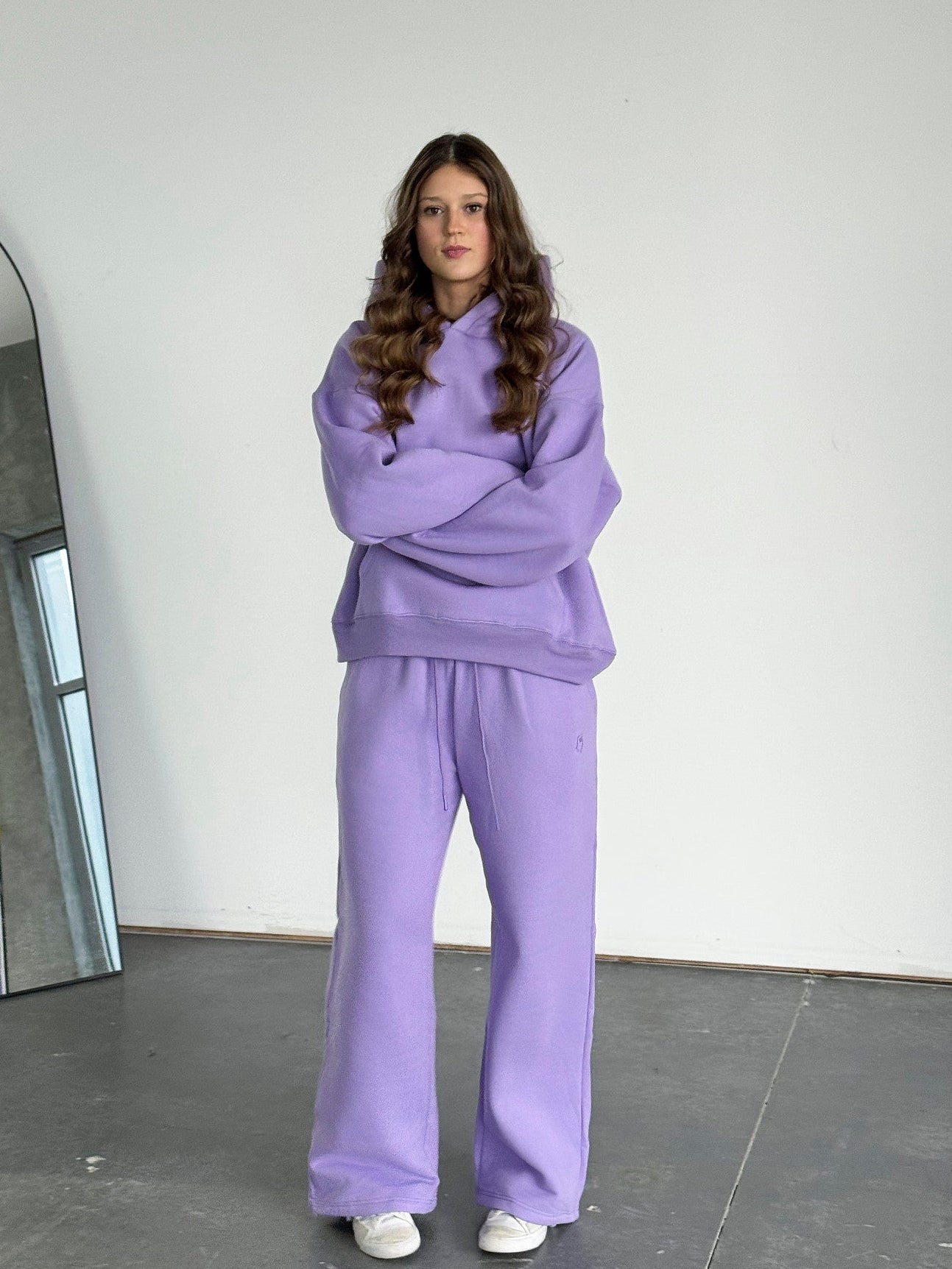 Person wearing a purple outfit standing in a minimalistic room with a large mirror.