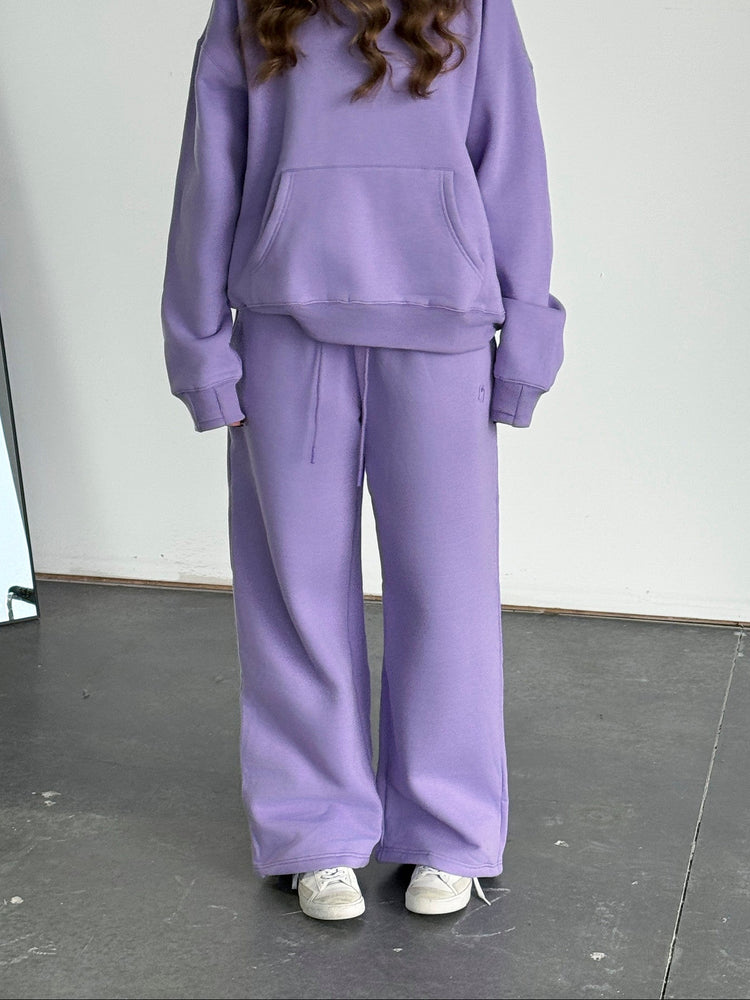 Person wearing a purple tracksuit standing against a white wall.