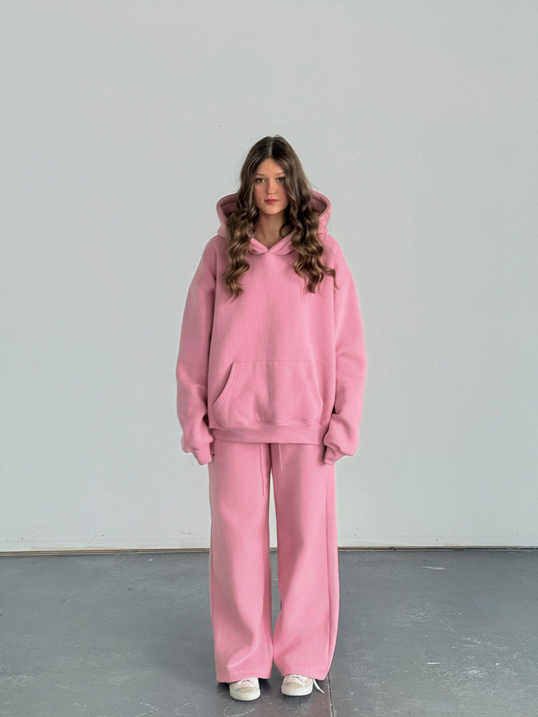 Person wearing a pink tracksuit standing against a plain background