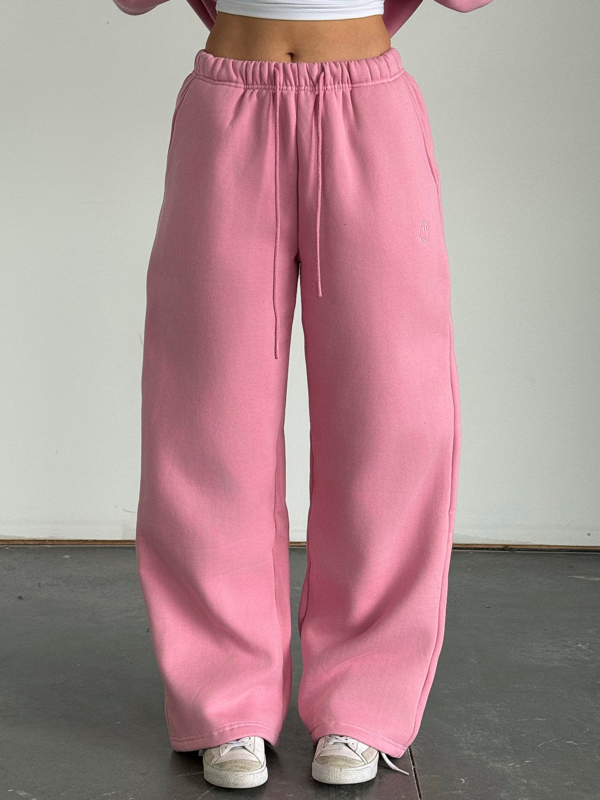 Person wearing a pink sweatshirt and pants with a white top against a plain background