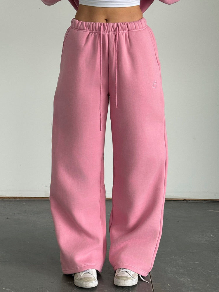 Person wearing a pink sweatshirt and pants with a white top against a plain background