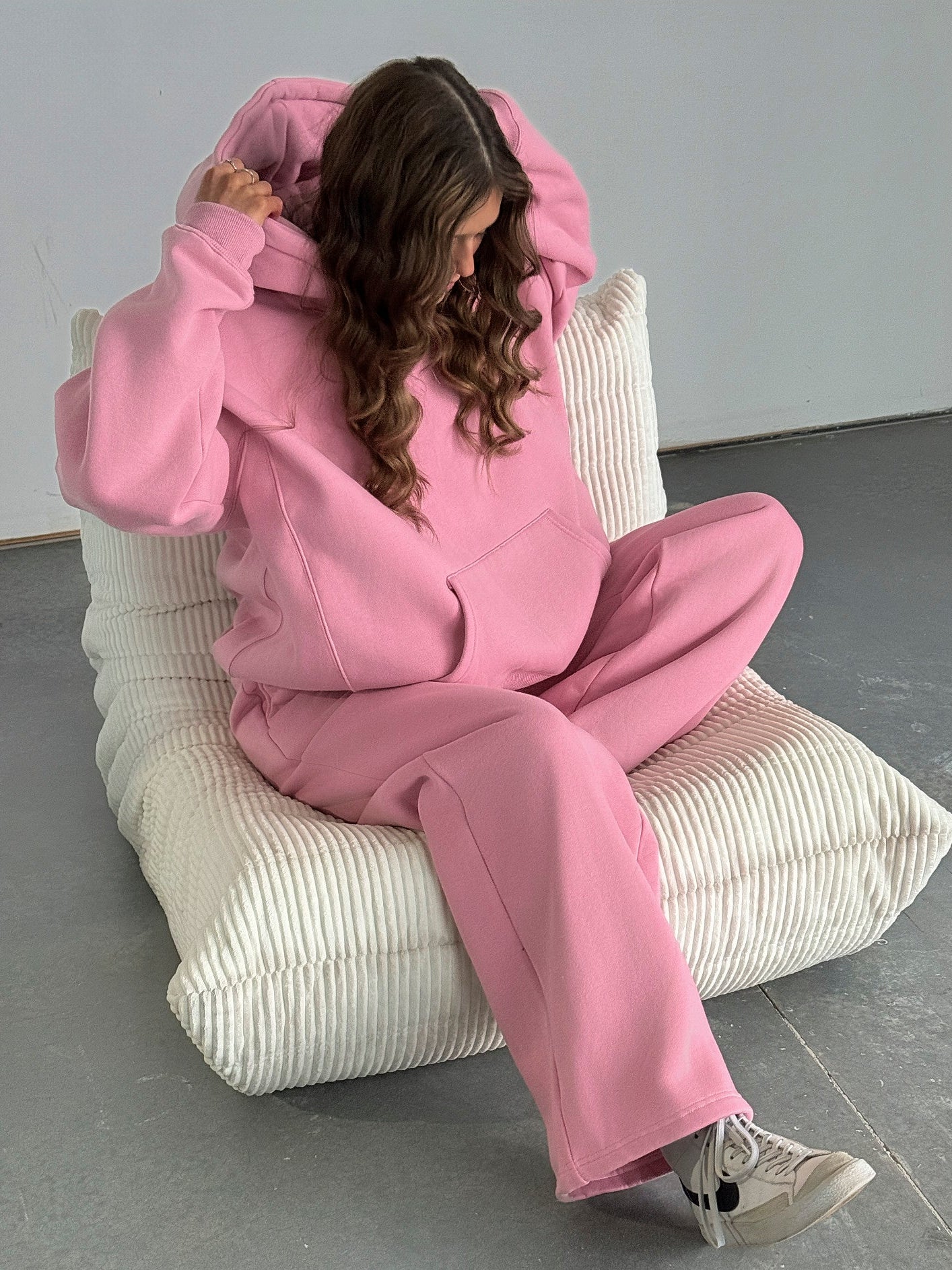 Person wearing a pink tracksuit sitting on a white chair against a gray background