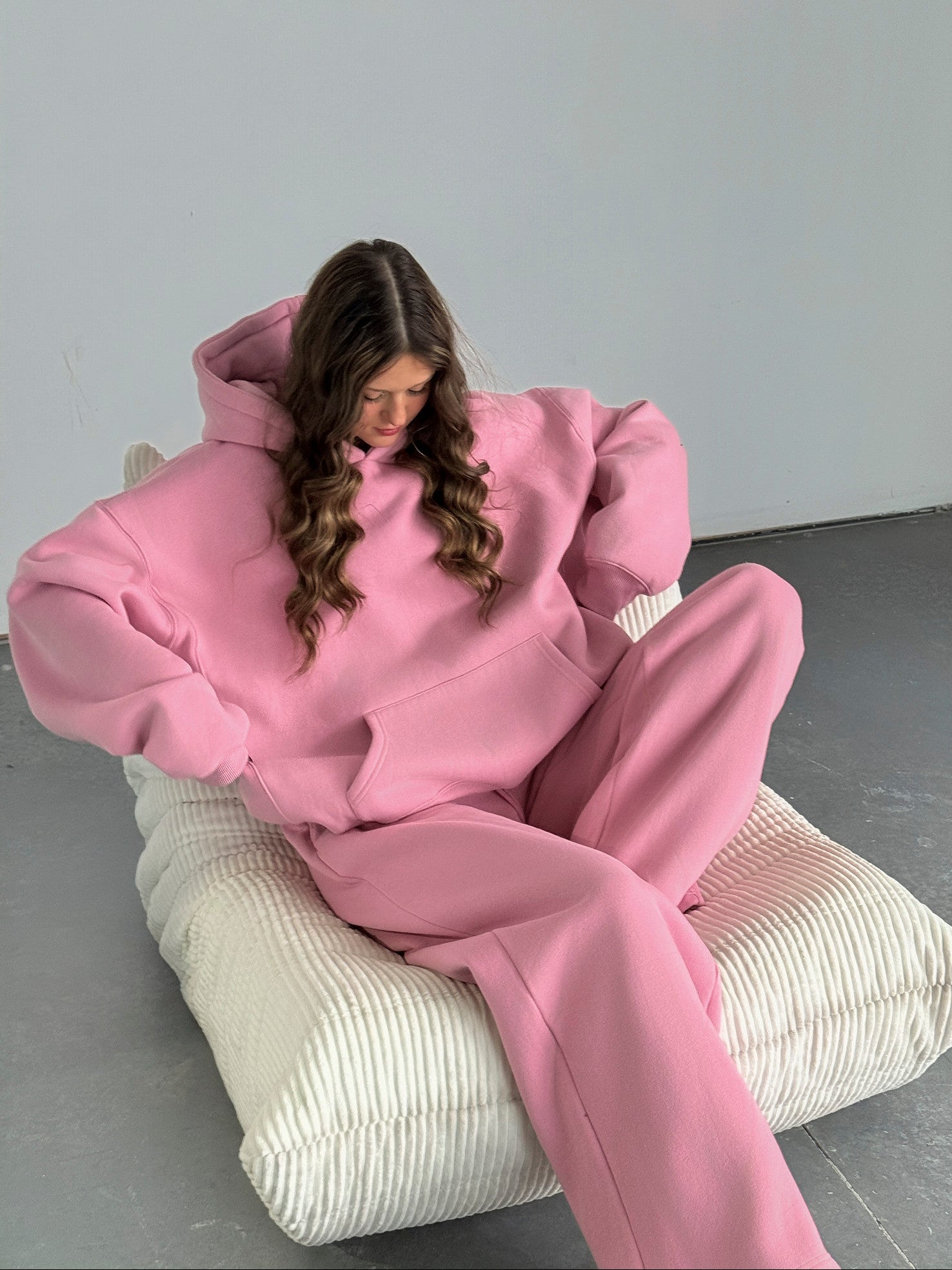 Person wearing a pink outfit sitting on a textured chair against a plain background