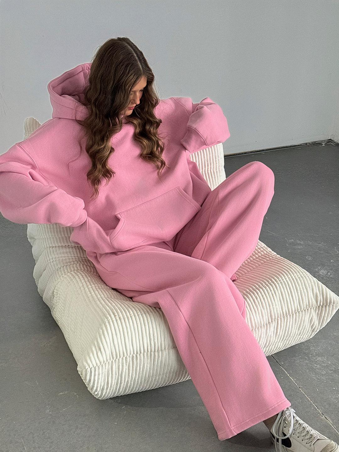 Person wearing a pink outfit sitting on a white chair against a gray background