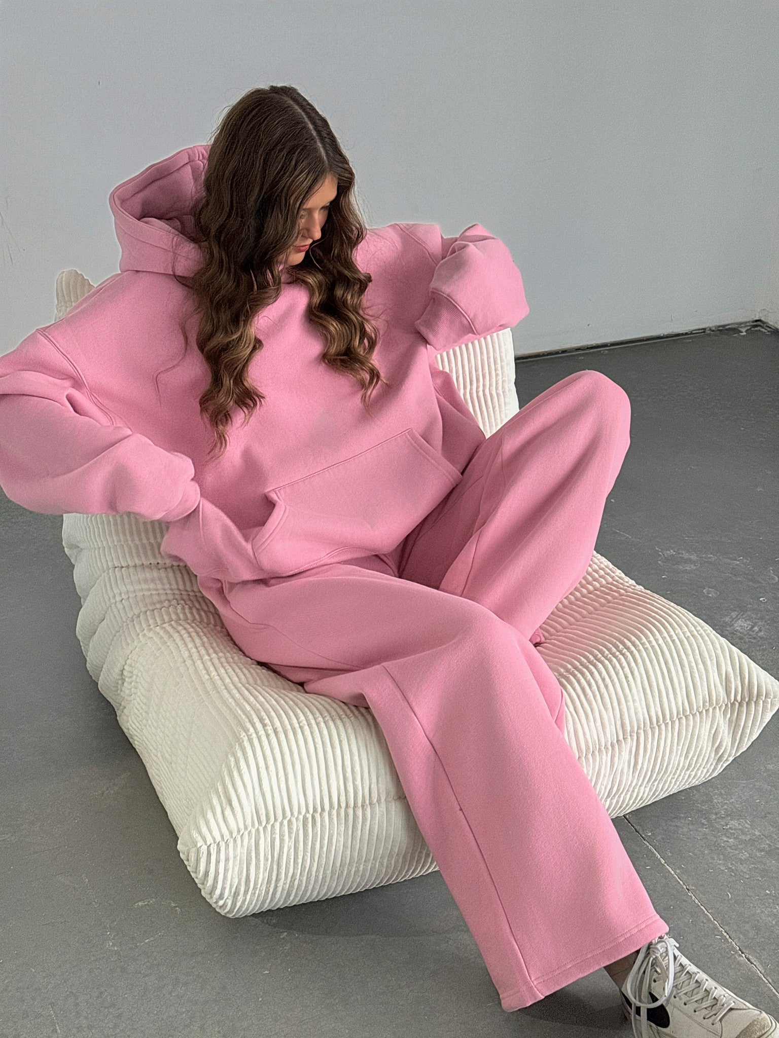 Person wearing a pink outfit sitting on a white chair against a gray background