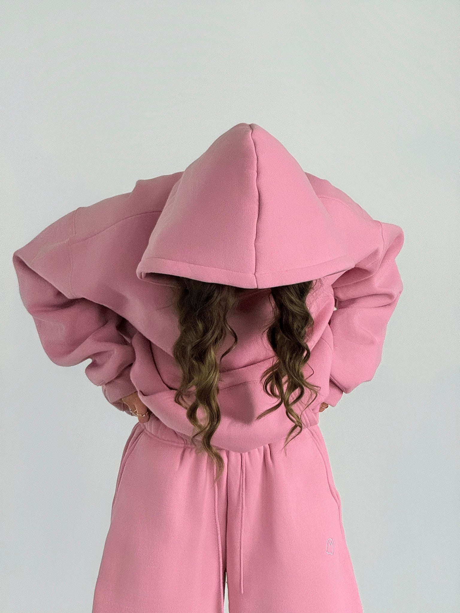 Person wearing a pink hoodie and pants against a white background