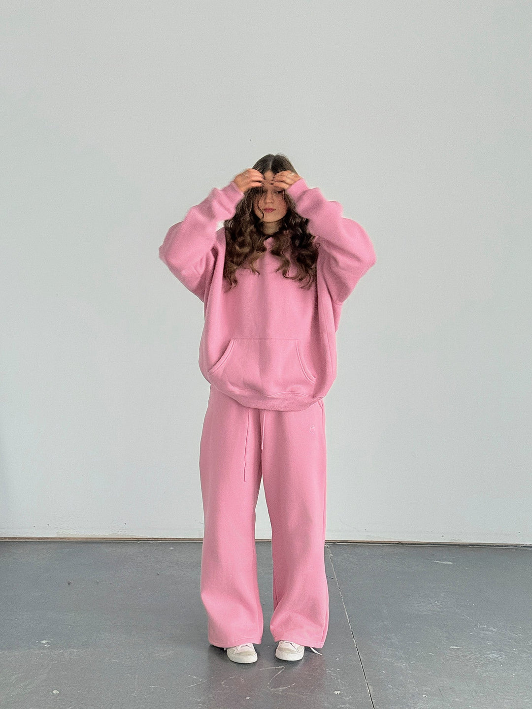 Person wearing a pink sweatshirt and pants standing against a white wall.