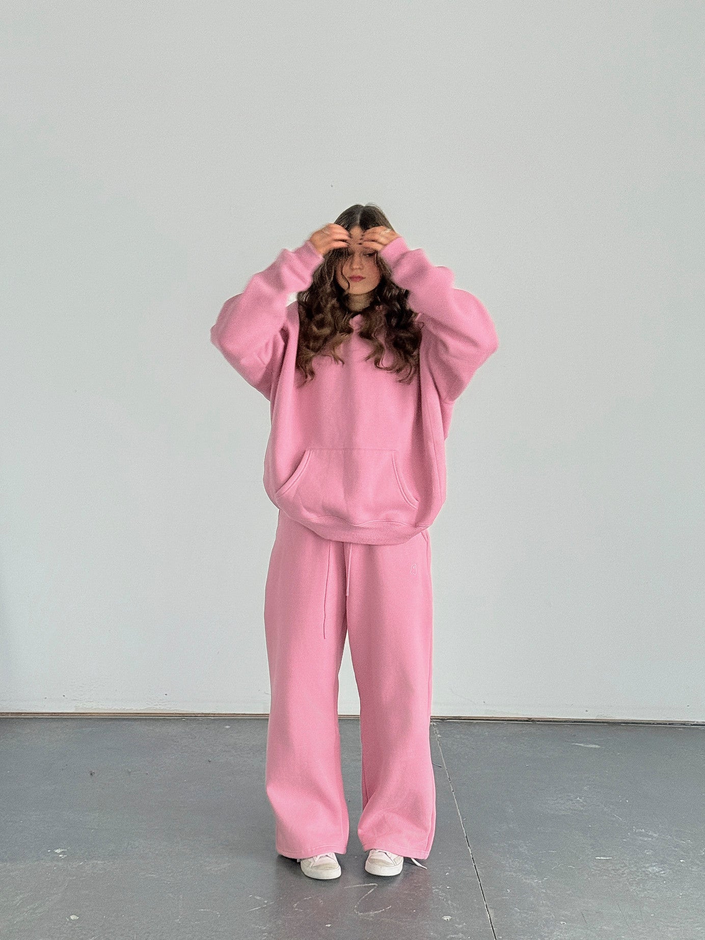 Person wearing a pink sweatshirt and pants standing against a white wall.