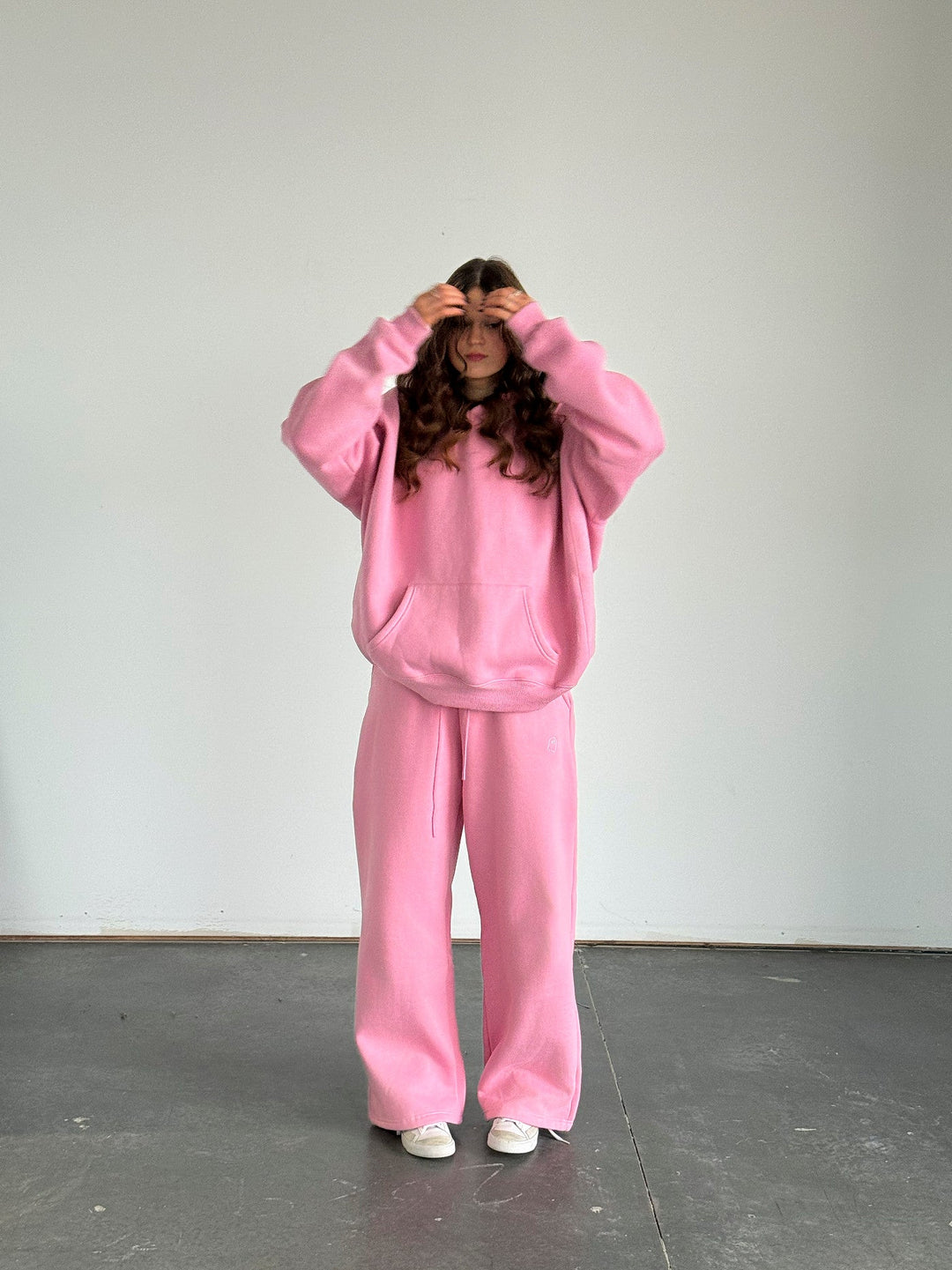 Person wearing a pink sweatshirt and pants set against a plain white wall.