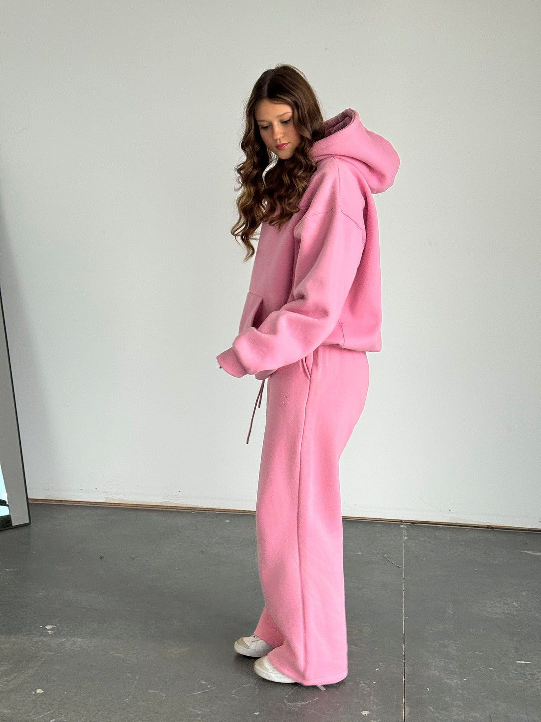 Person wearing a pink tracksuit standing against a plain white wall.
