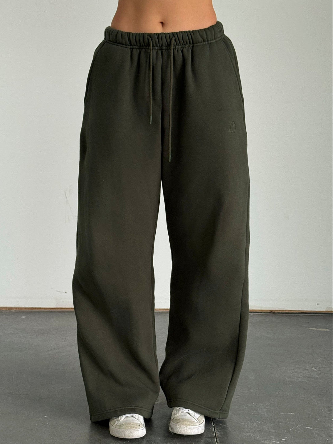 Person wearing olive green wide-leg pants with a white top on a plain background