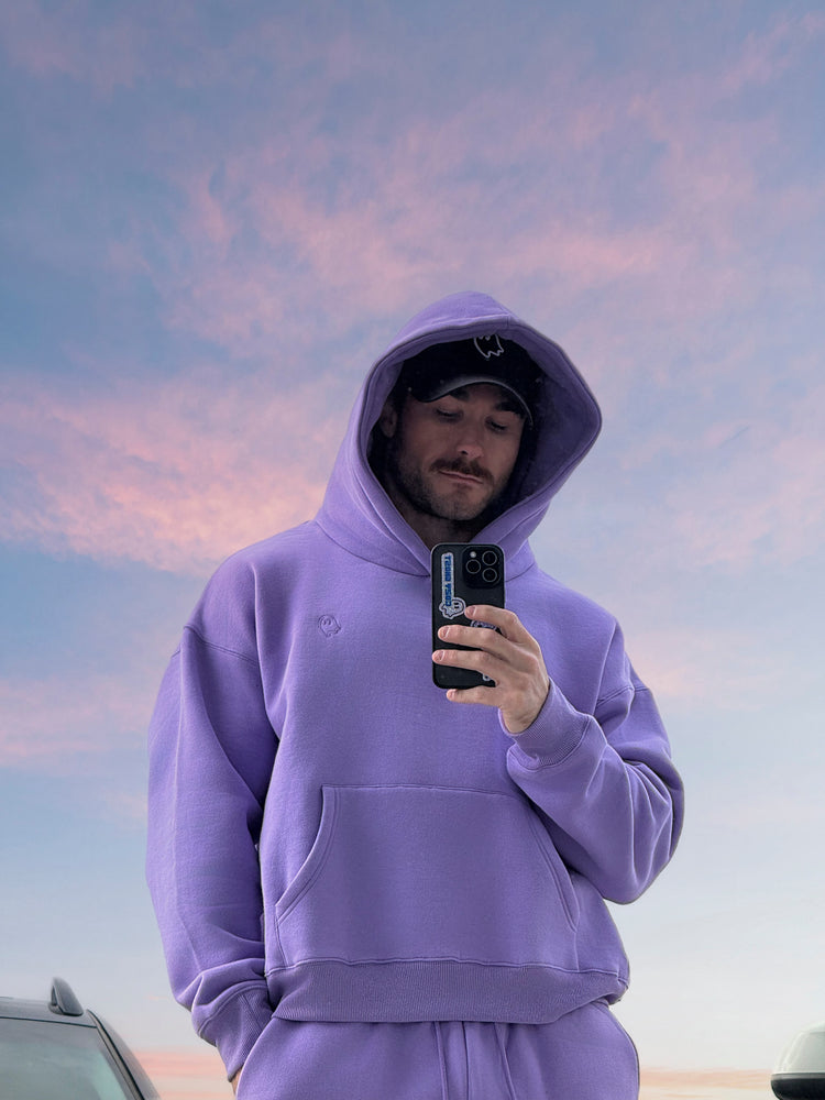 Person wearing a purple hoodie taking a selfie against a pink and blue sky.