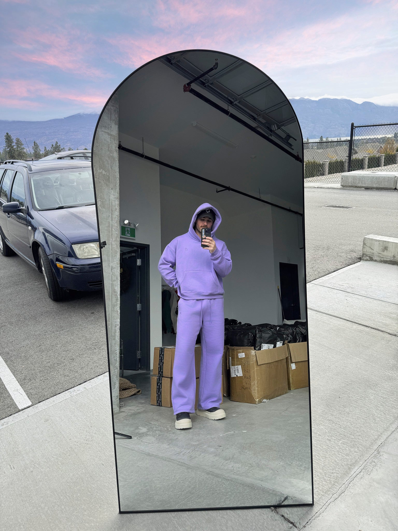 Person wearing a purple outfit taking a mirror selfie outdoors with mountains in the background.