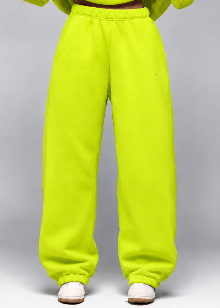A model wearing a matching neon yellow-green sweatshirt and sweatpants set, shown from the neck down against a neutral gray studio background.