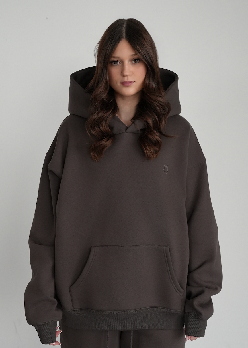 Person wearing a dark gray hoodie and pants on a light gray background