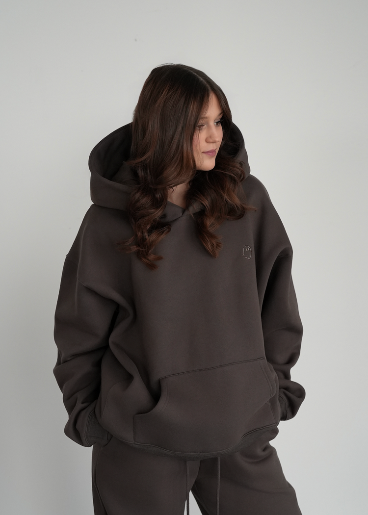 Person wearing a dark brown hoodie and pants against a plain background