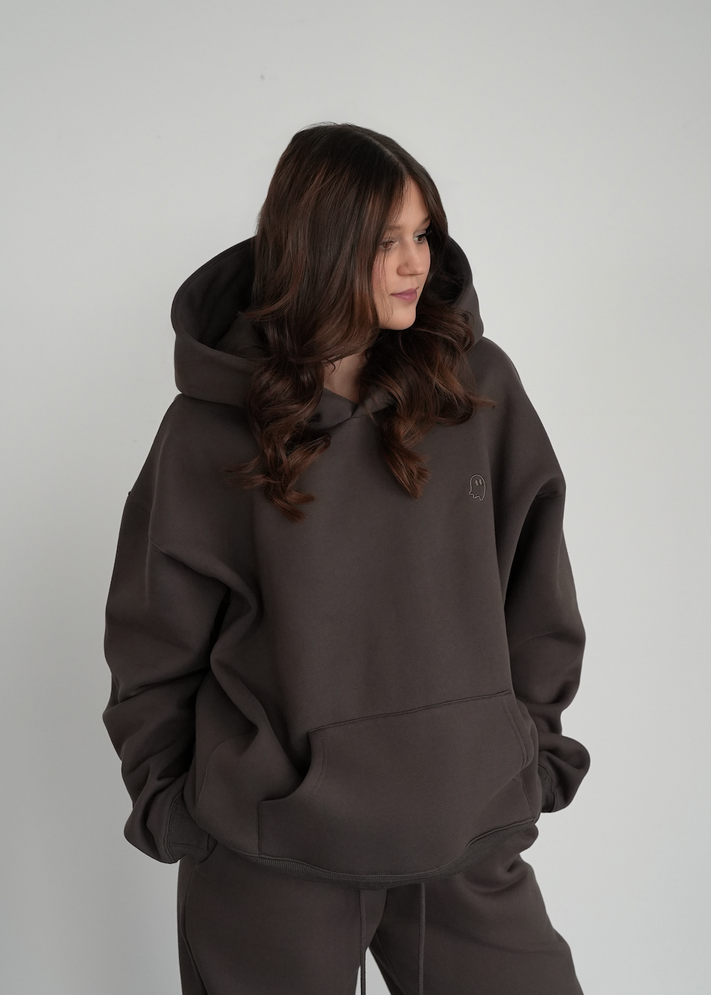 Person wearing a dark brown hoodie and pants against a plain background