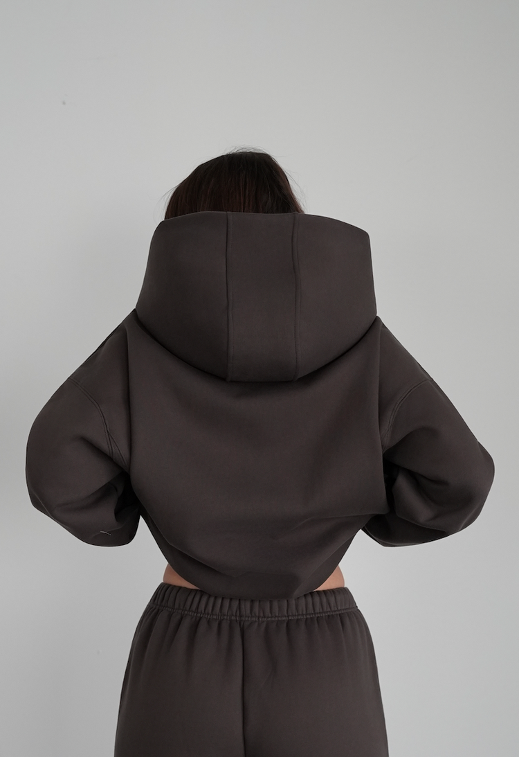 Person wearing a dark brown hoodie and pants on a light gray background