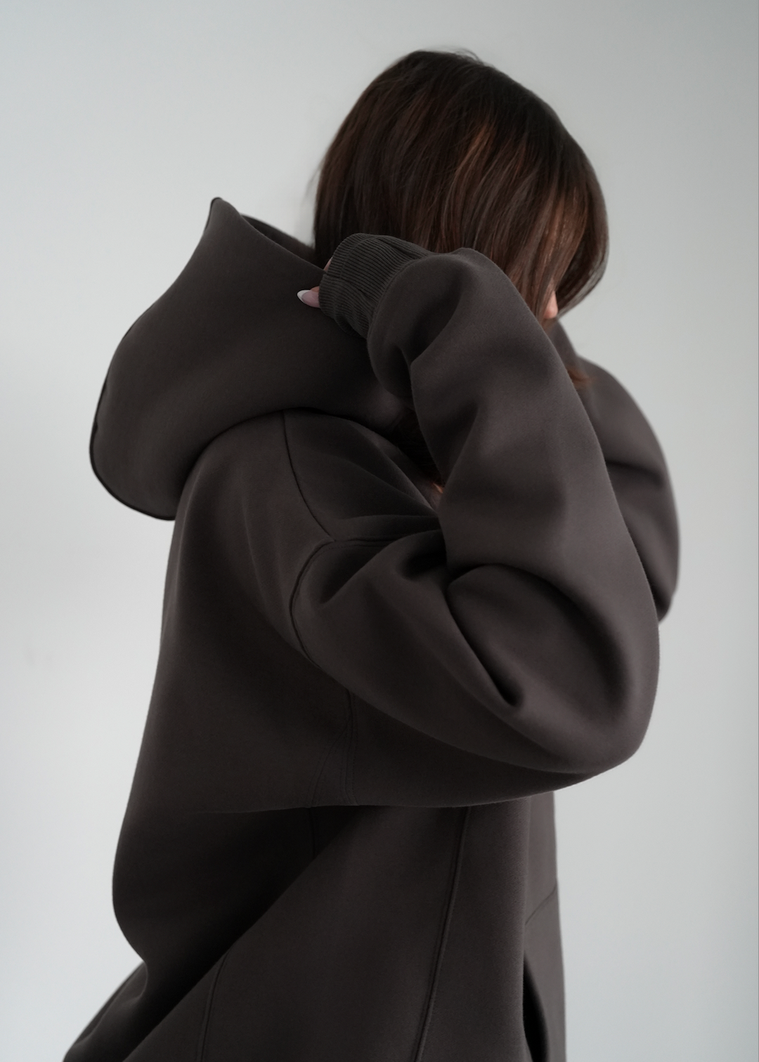 Person wearing a dark brown coat with their back to the camera on a plain background