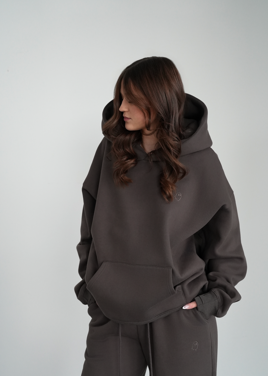 Person wearing a dark gray hoodie and pants on a light gray background