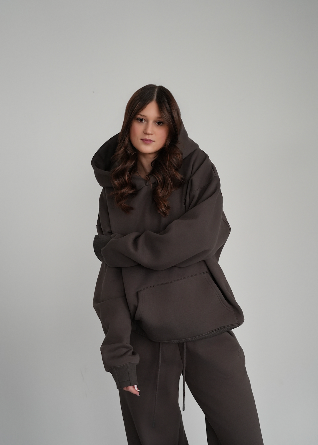 Person wearing a dark brown hoodie and pants on a light gray background