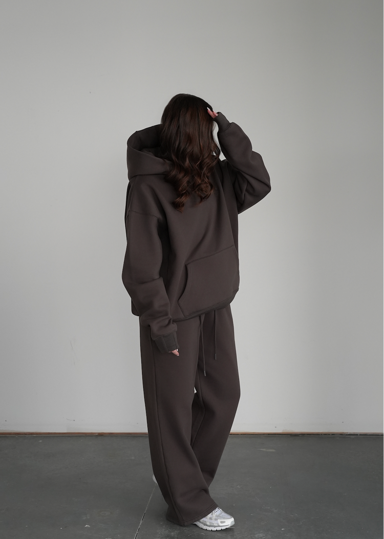 Person wearing a dark brown hoodie and pants against a plain background