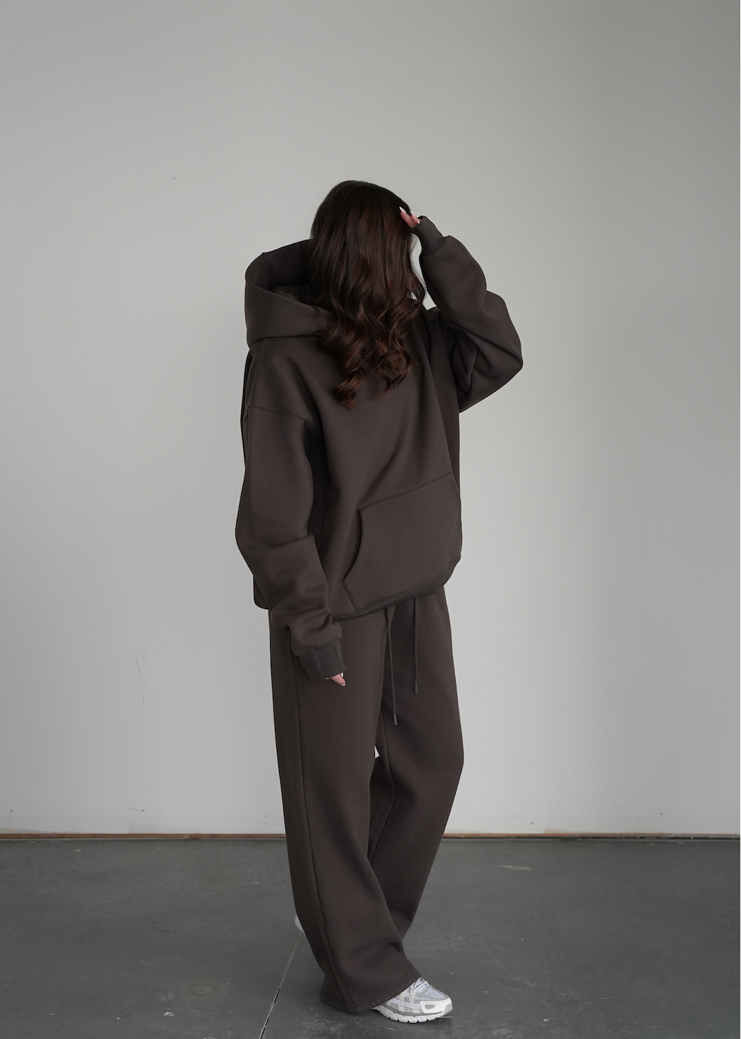 Person wearing a dark brown hoodie and pants against a plain background