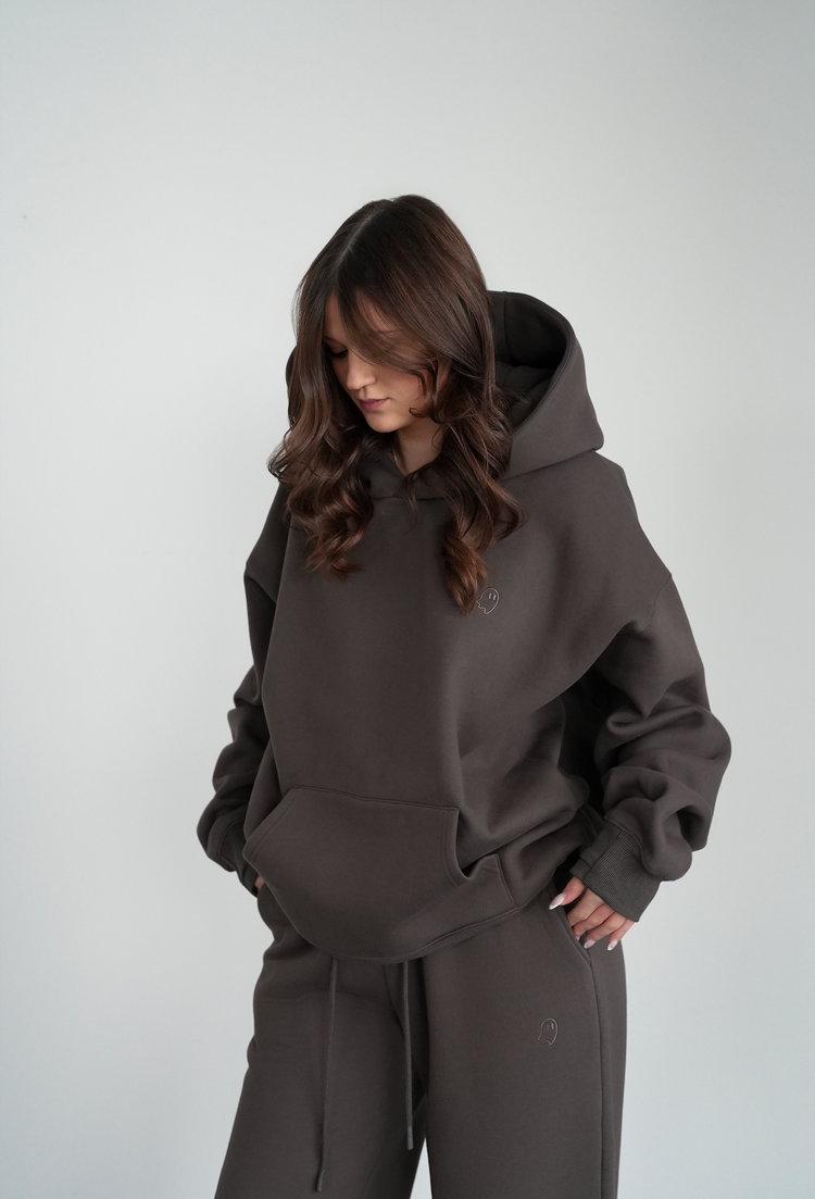 Person wearing a dark gray hoodie and pants on a light gray background