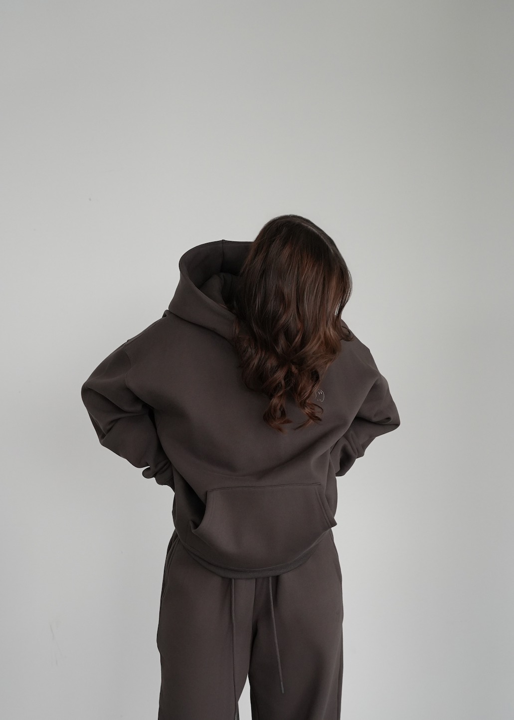 Person wearing a brown tracksuit against a plain white wall