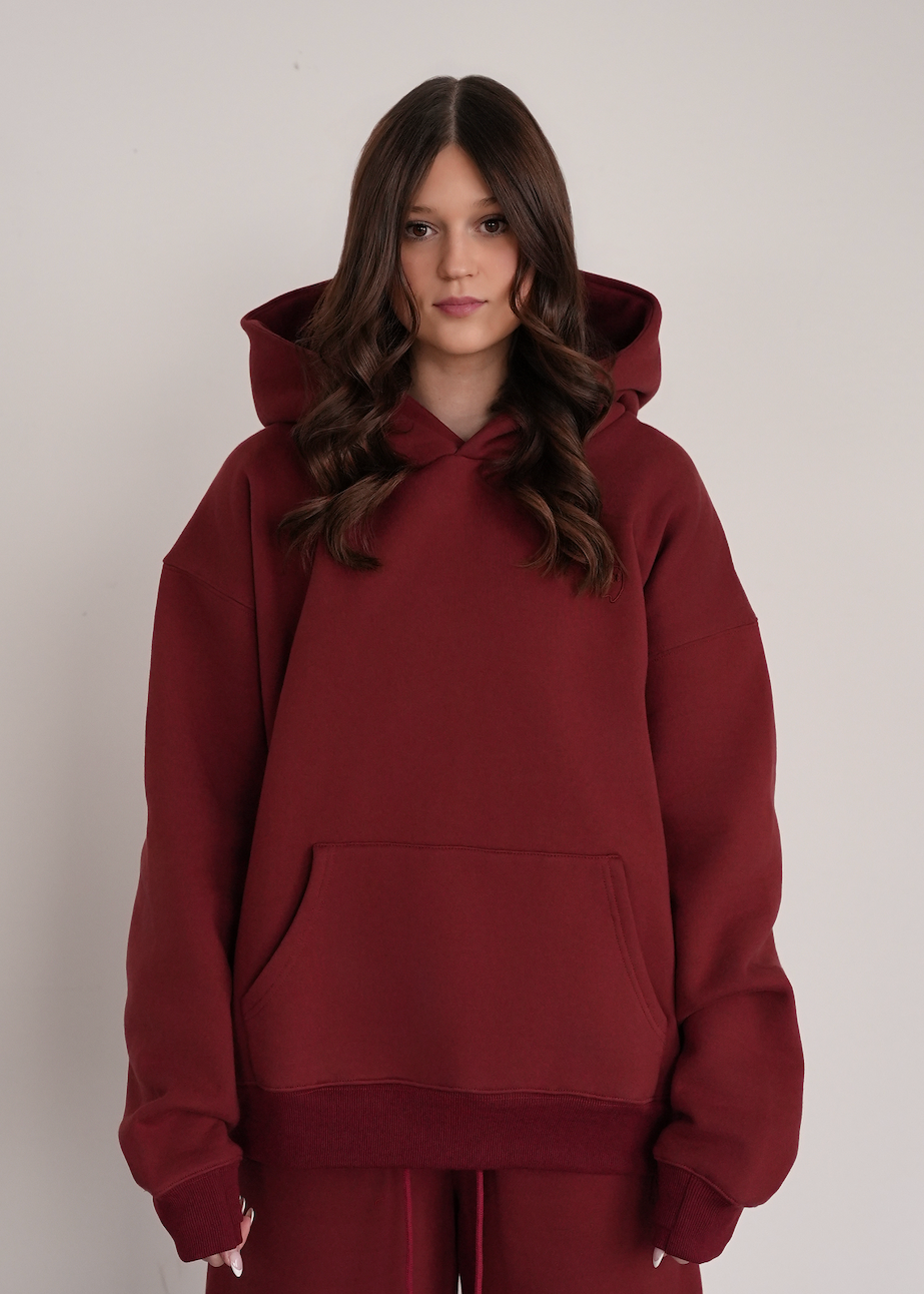 Person wearing a maroon hoodie and pants on a plain background