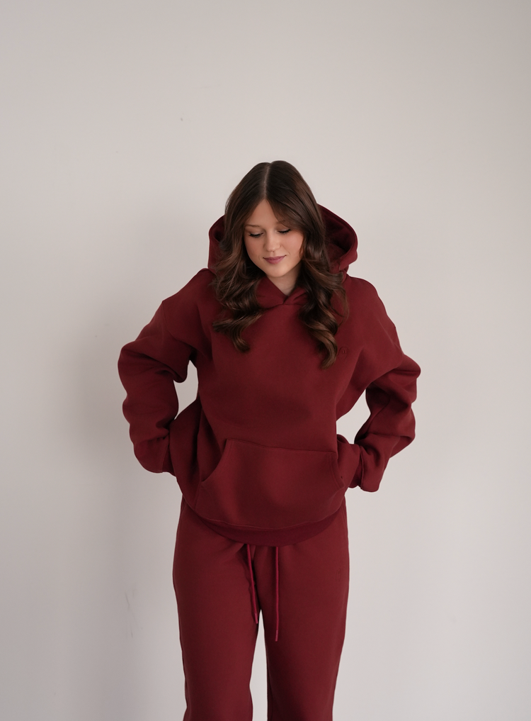 Person wearing a maroon hoodie and pants on a plain background