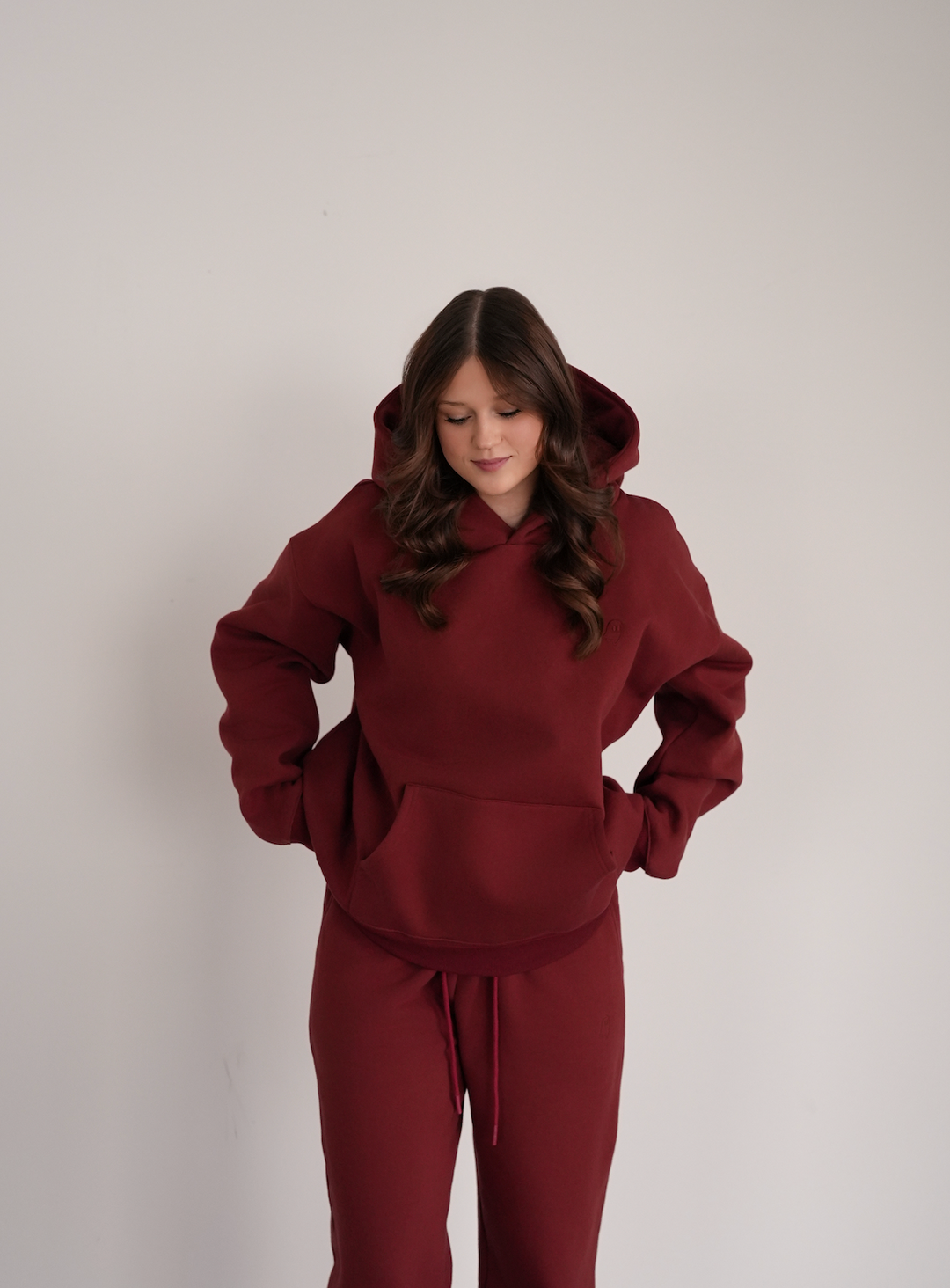 Person wearing a maroon hoodie and pants on a plain background
