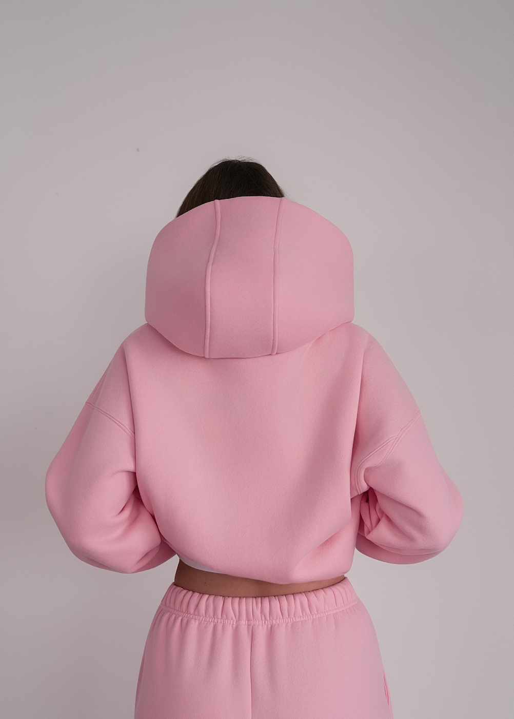 Person wearing a pink hoodie and pants against a plain background