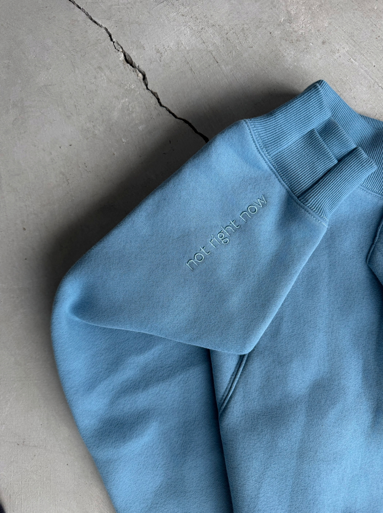 Blue sweatshirt with 'Right Now' text on a concrete surface