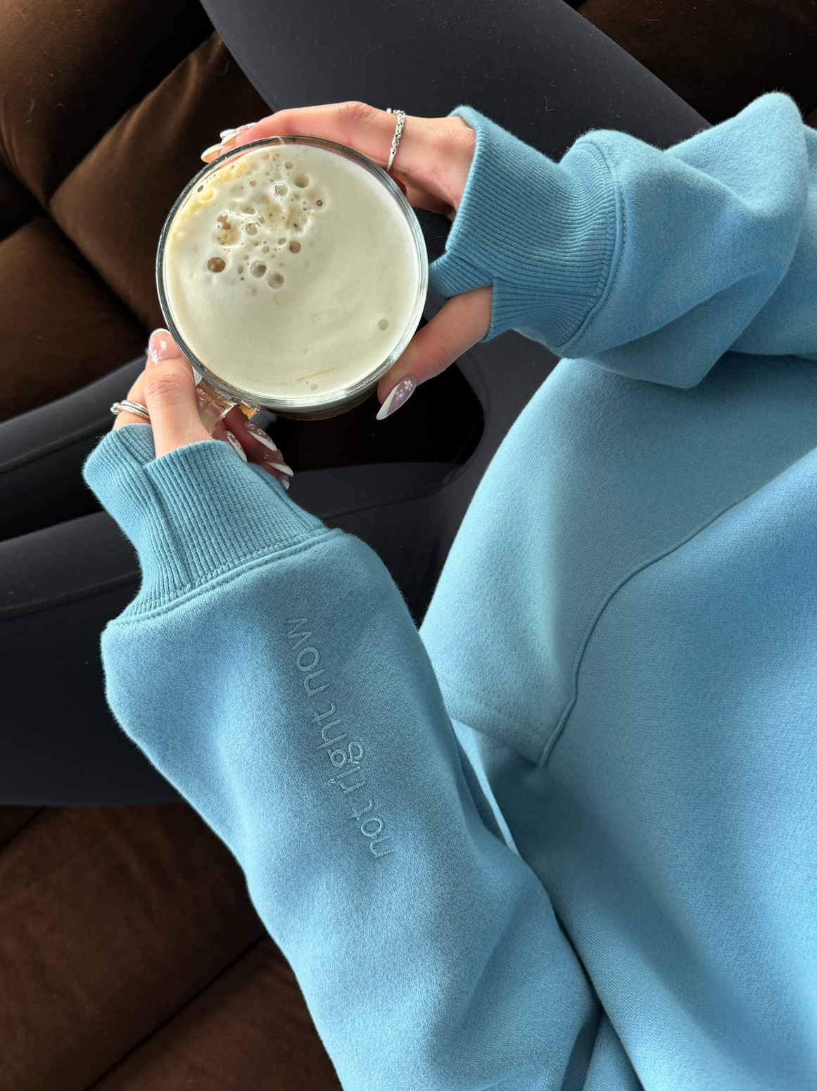 Person wearing a light blue sweatshirt holding a cup of coffee.