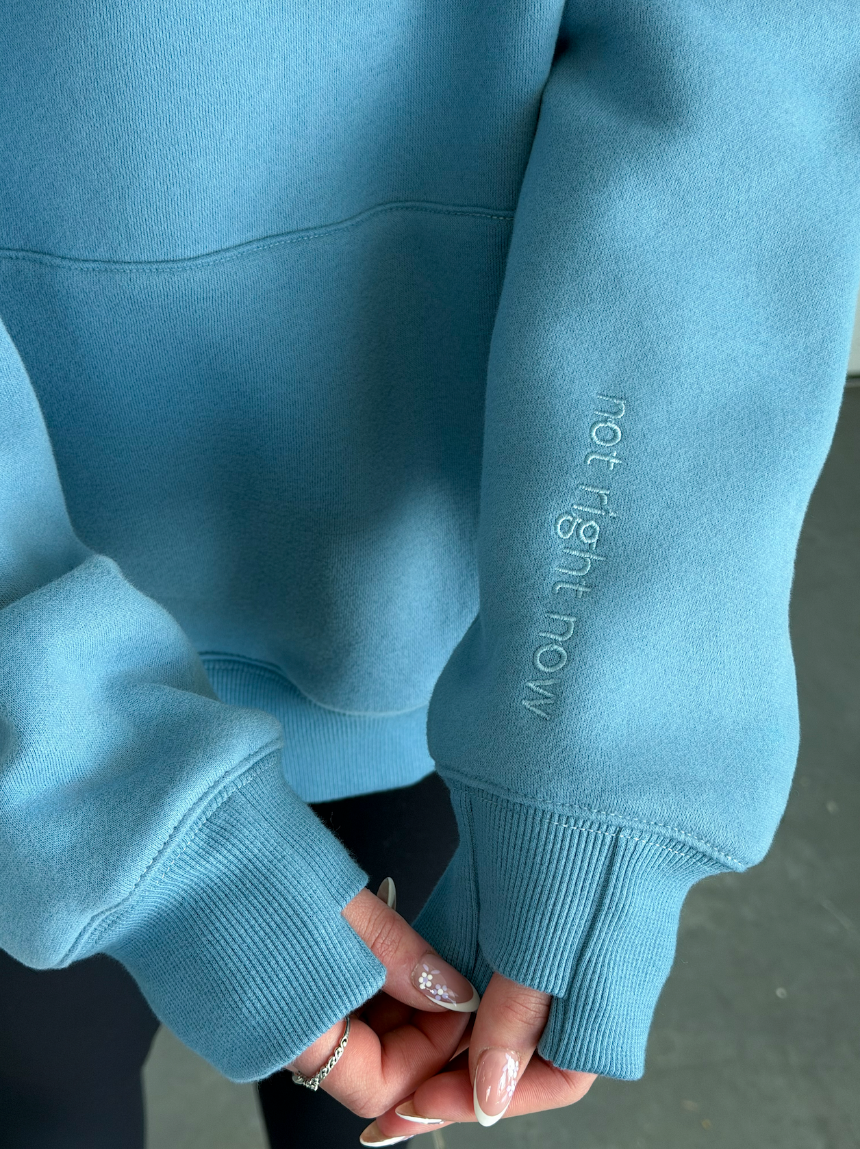 Light blue sweatshirt with text on sleeve held by a person against a neutral background